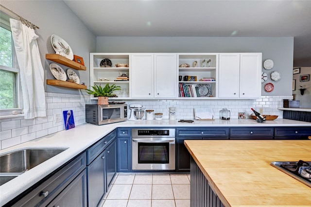 kitchen with stainless steel appliances, open shelves, blue cabinets, white cabinetry, and light tile patterned floors