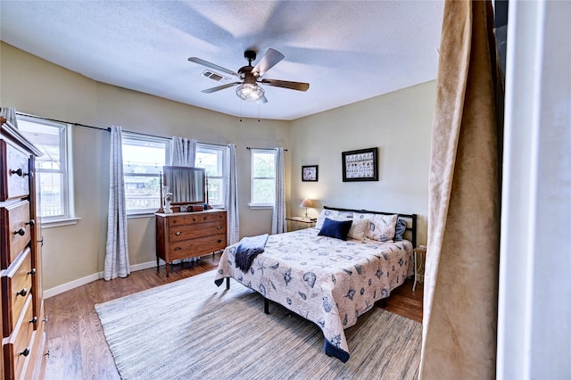 bedroom with wood finished floors, a textured ceiling, baseboards, and a ceiling fan