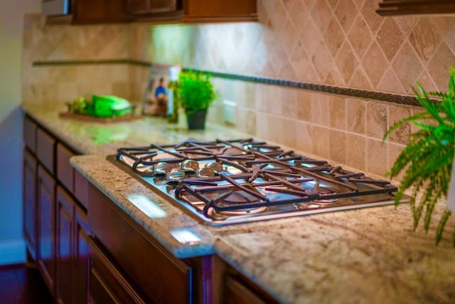 kitchen view of stainless steel gas stovetop, backsplash, light stone countertops, and brown cabinetry