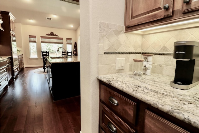 kitchen featuring decorative backsplash, a sink, light stone countertops, and dark wood-style flooring