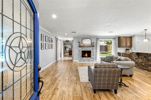 living room with light wood-style flooring, a textured ceiling, a lit fireplace, baseboards, and crown molding