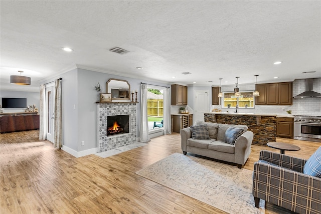 living area with light wood-style floors, a fireplace, ornamental molding, recessed lighting, and baseboards