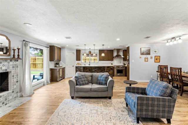 living area featuring crown molding, a textured ceiling, light wood-style flooring, a tiled fireplace, and recessed lighting