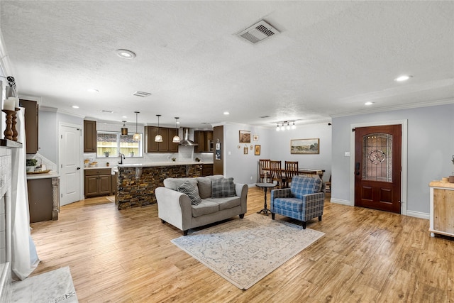 living room with ornamental molding, a textured ceiling, recessed lighting, light wood-style flooring, and baseboards