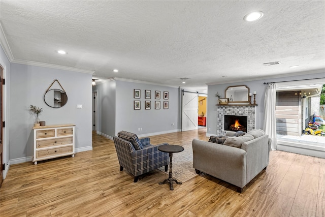 living area featuring a barn door, light wood-style floors, ornamental molding, recessed lighting, and a textured ceiling