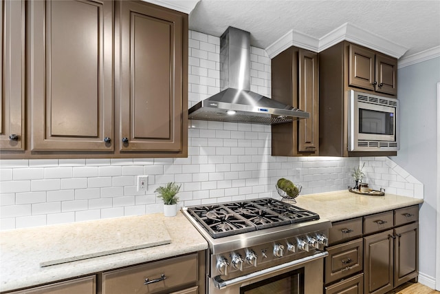kitchen featuring stainless steel appliances, wall chimney exhaust hood, crown molding, tasteful backsplash, and dark brown cabinetry
