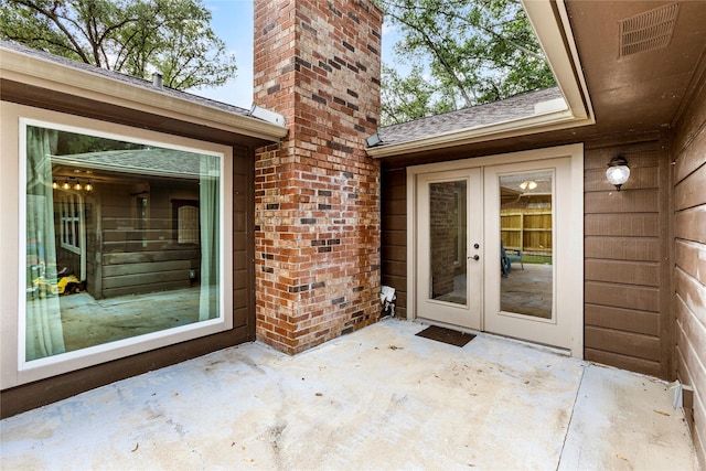 doorway to property featuring french doors, a shingled roof, a patio area, a chimney, and brick siding