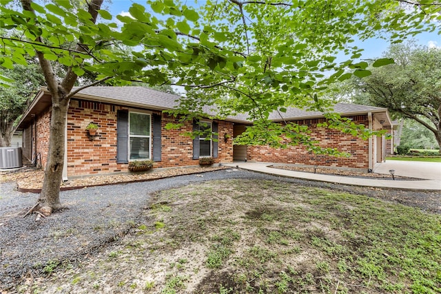 ranch-style home featuring central AC, brick siding, roof with shingles, and driveway