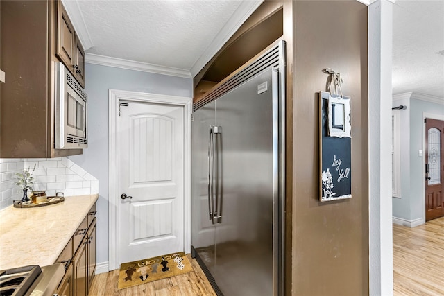 kitchen with built in appliances, light wood-style floors, a textured ceiling, tasteful backsplash, and ornamental molding