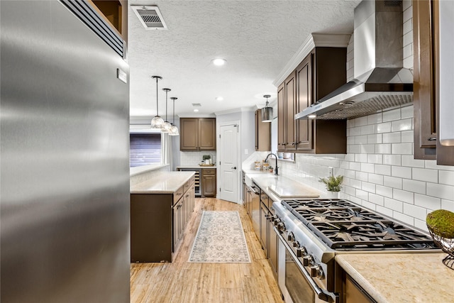 kitchen featuring premium appliances, wall chimney range hood, light wood-style floors, pendant lighting, and backsplash