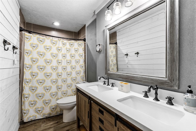 bathroom with wood finished floors, a textured ceiling, toilet, double vanity, and a shower with shower curtain