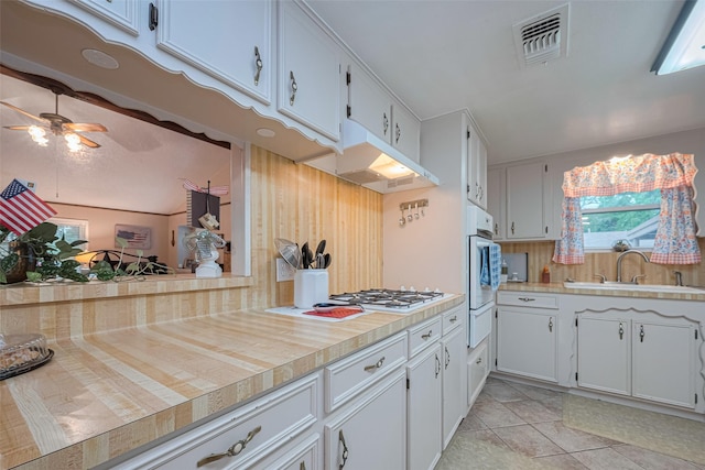 1745 15th St, Hempstead, TX 77445 - kitchen with light countertops, white cabinets, ceiling fan, under cabinet range hood, and a sink