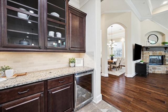bar featuring wine cooler, crown molding, a chandelier, arched walkways, and baseboards