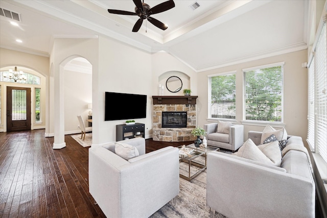 living area with hardwood / wood-style flooring, crown molding, a stone fireplace, arched walkways, and baseboards