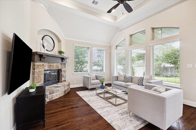 living area featuring ceiling fan, dark wood-style flooring, a stone fireplace, ornamental molding, and baseboards