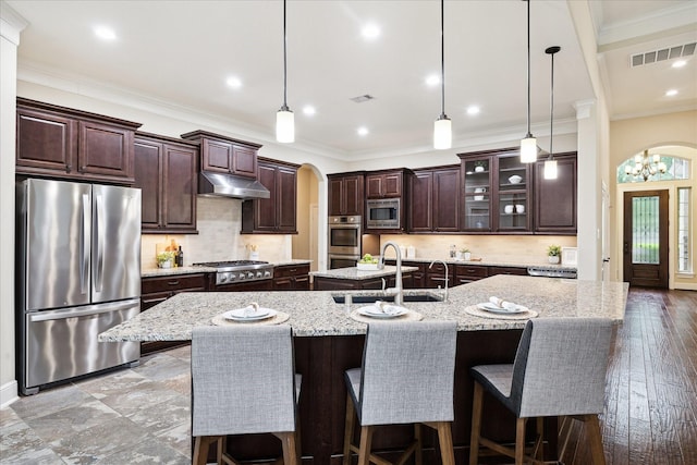 kitchen featuring stainless steel appliances, a sink, arched walkways, a large island with sink, and under cabinet range hood