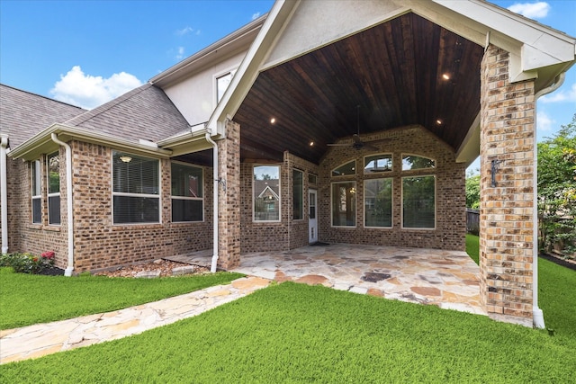 rear view of property with ceiling fan, a patio area, a yard, brick siding, and roof with shingles