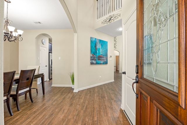 entrance foyer featuring a chandelier, arched walkways, dark wood-type flooring, and baseboards