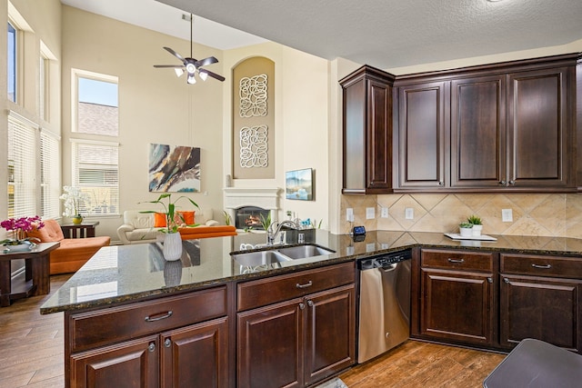 kitchen with dishwasher, a sink, dark wood-type flooring, open floor plan, and dark stone countertops