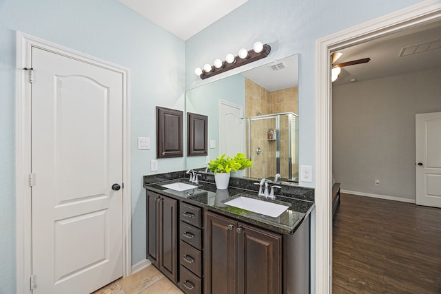 bathroom with a stall shower, baseboards, double vanity, a ceiling fan, and wood finished floors