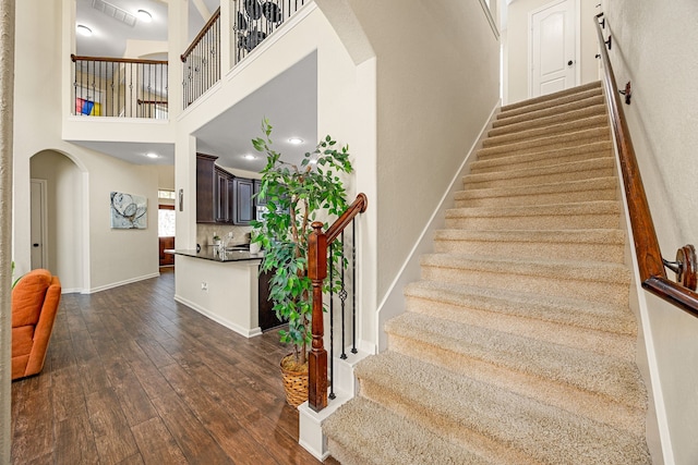 stairway featuring arched walkways, hardwood / wood-style floors, baseboards, and a high ceiling