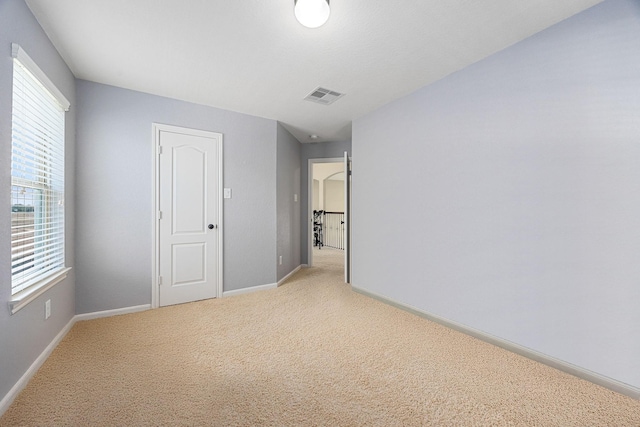 spare room featuring healthy amount of natural light, light carpet, and baseboards