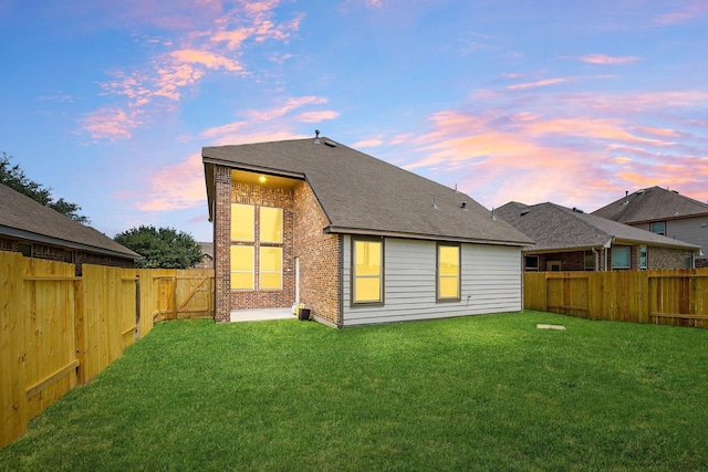 back of house at dusk featuring brick siding and a shingled roof