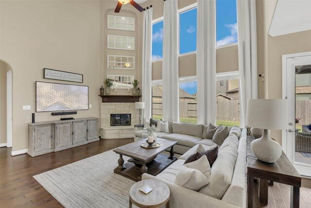 17306 Legend Brook Ct, Tomball, TX 77375 - living room featuring arched walkways, a ceiling fan, a towering ceiling, a fireplace, and dark wood-style flooring