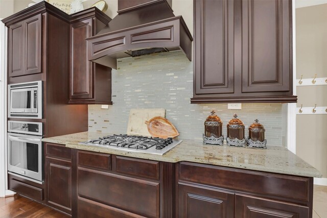 17306 Legend Brook Ct, Tomball, TX 77375 - kitchen featuring appliances with stainless steel finishes, custom exhaust hood, dark brown cabinetry, and decorative backsplash