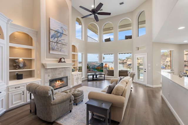 44 Logansport Ct, Montgomery, TX 77356 - living room featuring a glass covered fireplace, ceiling fan, dark wood-style floors, built in shelves, and a towering ceiling