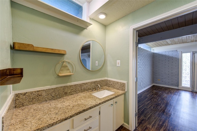 bathroom with brick wall, wood finished floors, baseboards, beam ceiling, and vanity