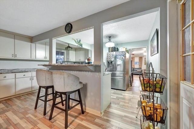 7027 Iowa Colony Blvd, Rosharon, TX 77583 - kitchen with stainless steel refrigerator with ice dispenser, a kitchen breakfast bar, white cabinetry, light wood finished floors, and light stone counters