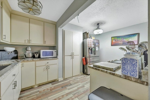 7027 Iowa Colony Blvd, Rosharon, TX 77583 - kitchen with stainless steel fridge, white microwave, cream cabinetry, light wood-type flooring, and a textured ceiling