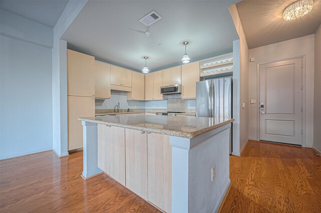 kitchen featuring appliances with stainless steel finishes, light wood finished floors, a center island, light stone countertops, and a sink