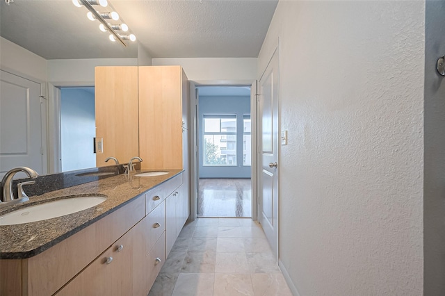 bathroom with a textured wall, baseboards, double vanity, and a textured ceiling