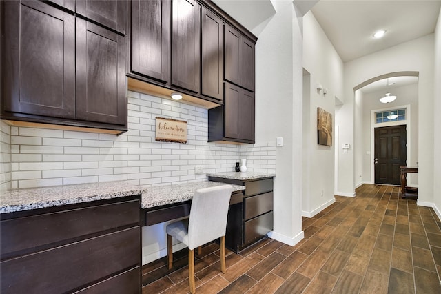 16711 Ramsay Cascades Dr, Humble, TX 77346 - kitchen with dark brown cabinets, light stone countertops, arched walkways, backsplash, and baseboards