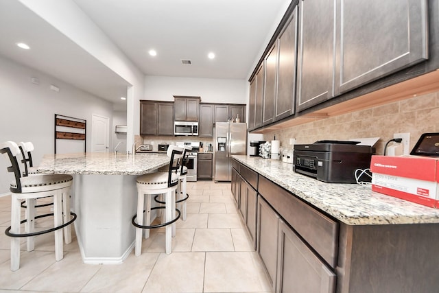 4827 San Gregorio Ln, Katy, TX 77493 - kitchen featuring stainless steel appliances, a breakfast bar area, decorative backsplash, dark brown cabinets, and light tile patterned floors