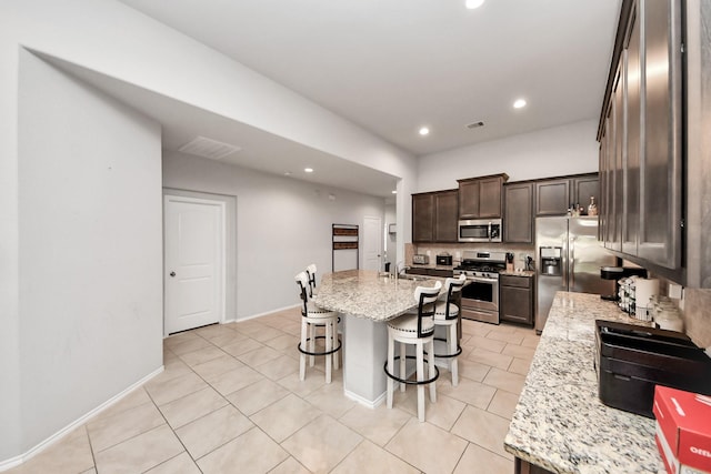 4827 San Gregorio Ln, Katy, TX 77493 - kitchen with stainless steel appliances, a kitchen bar, light tile patterned floors, dark brown cabinets, and an island with sink
