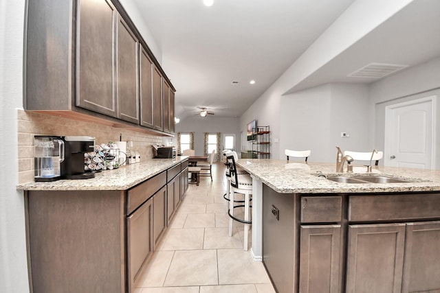 4827 San Gregorio Ln, Katy, TX 77493 - kitchen featuring a sink, light tile patterned floors, a breakfast bar, ceiling fan, and light stone counters