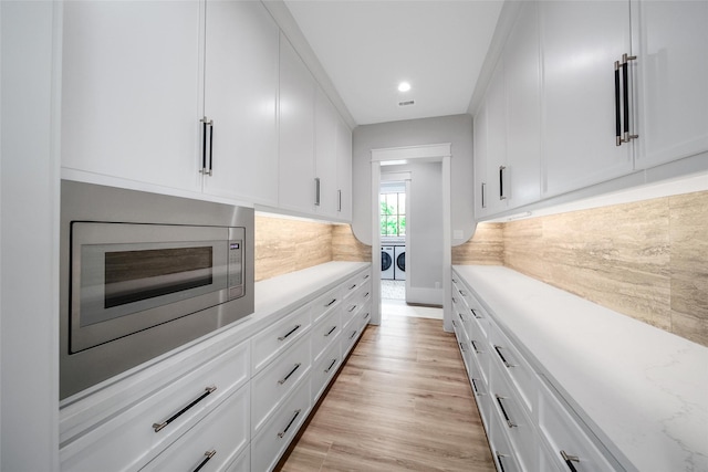 18829 Cypress Church Rd, Cypress, TX 77433 - kitchen featuring separate washer and dryer, stainless steel microwave, tasteful backsplash, white cabinetry, and light wood-style flooring