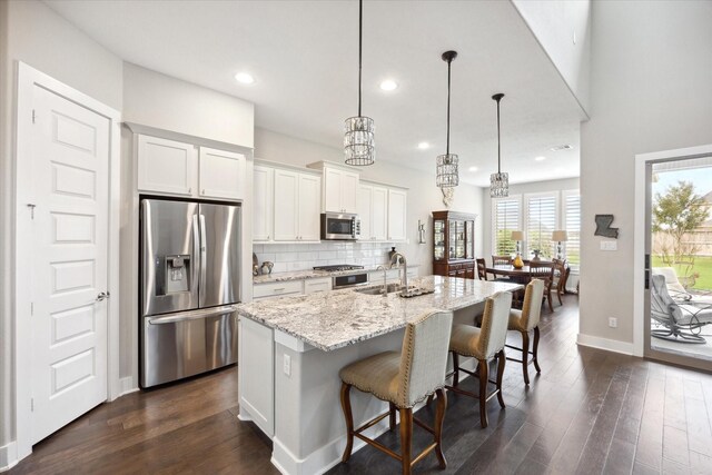 809 Stella Vista Ct, Katy, TX 77493 - kitchen featuring stainless steel appliances, dark wood-type flooring, a kitchen island with sink, white cabinetry, and a breakfast bar