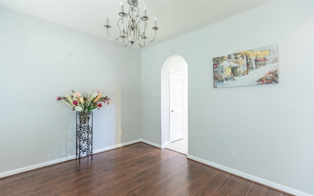 unfurnished dining area with arched walkways, a chandelier, wood-type flooring, and baseboards