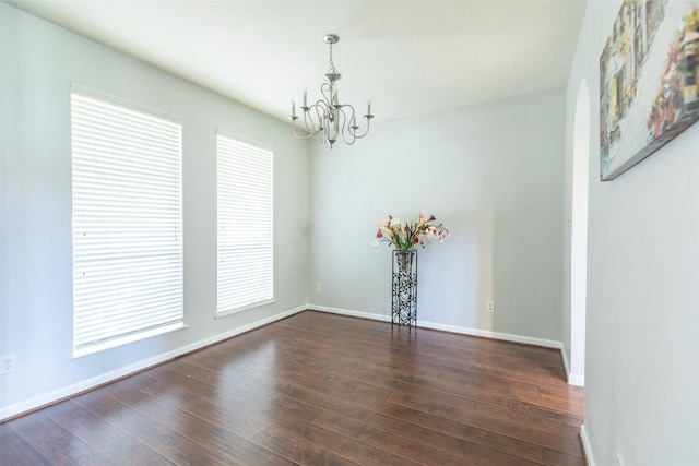 spare room with a chandelier, dark wood finished floors, and baseboards