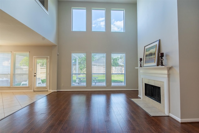 unfurnished living room featuring a fireplace, baseboards, a high ceiling, plenty of natural light, and wood finished floors