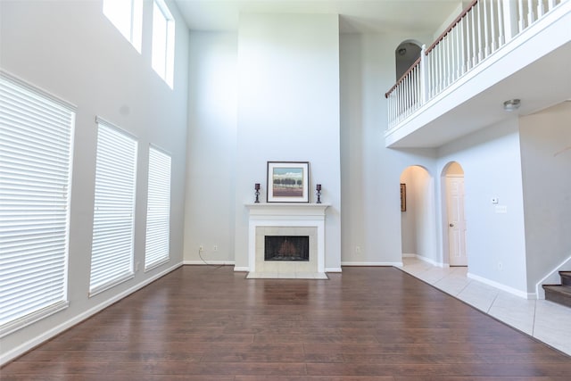 unfurnished living room featuring a towering ceiling, arched walkways, hardwood / wood-style flooring, stairway, and a tiled fireplace