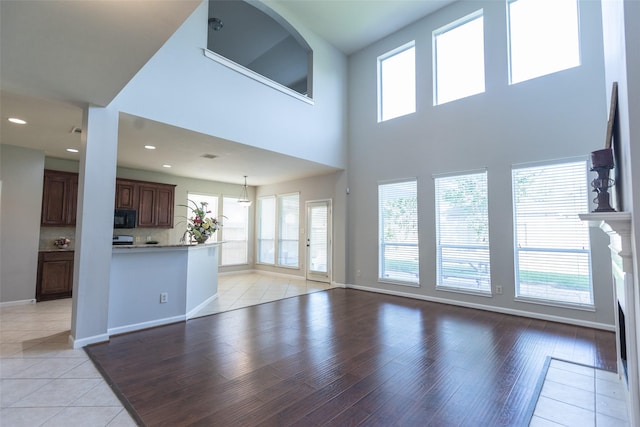 unfurnished living room with healthy amount of natural light, light wood-style floors, baseboards, recessed lighting, and a high ceiling