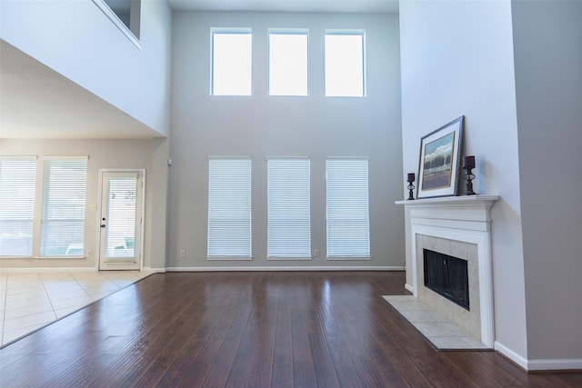 unfurnished living room featuring a fireplace, a high ceiling, baseboards, healthy amount of natural light, and wood finished floors
