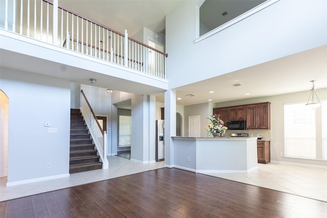 unfurnished living room featuring light wood-style flooring, arched walkways, a towering ceiling, and baseboards