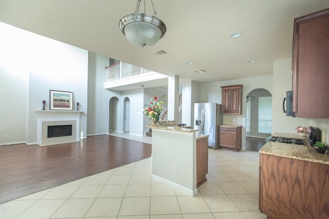 kitchen featuring stainless steel fridge, range with gas cooktop, arched walkways, black microwave, and a fireplace with flush hearth