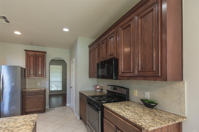 kitchen with appliances with stainless steel finishes, arched walkways, decorative backsplash, light tile patterned floors, and light stone counters